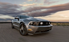 Серебристый Ford Mustang влетает на скорости в поворот под вечерним небом